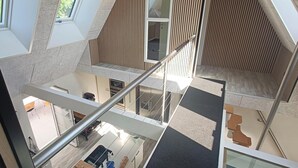 Ein mehrgeschossiges Interieur mit einer Treppe, Blick auf einen Raum darunter und einer Wand aus Holzlamellen.