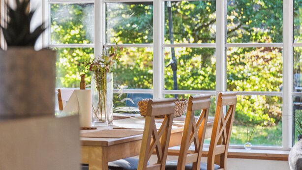Ein Zimmer mit großem Fenster, Holzstühlen, einem Tisch und einem Blumentopf.