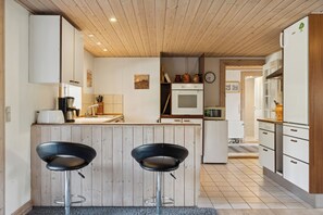 A modern kitchen with wooden cabinets, a central island with stools, a microwave, and a refrigerator.