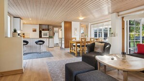 Ein modernes Interieur mit Holzbalkendecke, einem Essbereich, einer Küche und einem Wohnbereich mit Sofa und Hocker.