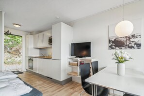 A modern kitchen with white cabinets, a flat-screen TV, and a dining area with a white table and chairs. - Lovely holiday apartment consumption included (Allinge)