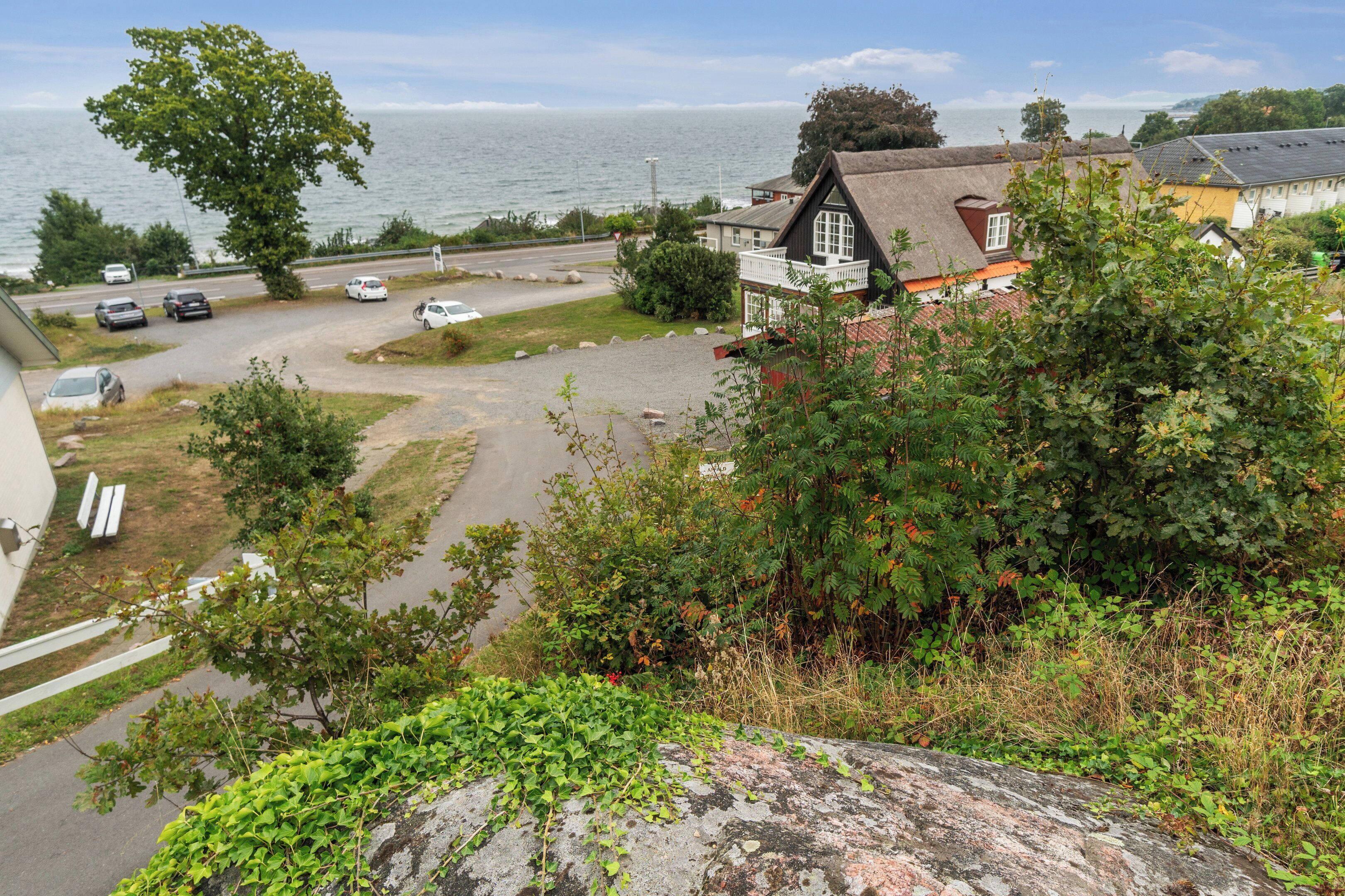 En fastighet vid kusten med ett hus med halmtak, en uppfart och utsikt över havet.