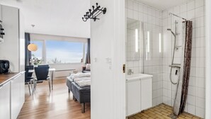 Una habitación de hotel moderna con ducha, cama, zona de comedor y vistas al cielo.