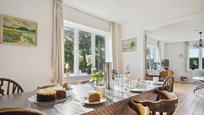 En matplats med ett bord dukat för fyra personer, stolar, ett fönster med gardiner och utsikt över grönområden utanför.