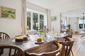 A dining area with a table set for four, chairs, a window with curtains, and a view of greenery outside. - 750 m2 countryside idyll with activity room (Haderslev)