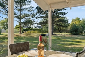 Uma área de estar coberta ao ar livre com mesa, cadeiras e uma garrafa de vinho.