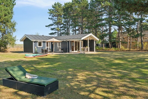 A house with a covered patio, a lawn, and a lounge chair.