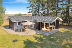 A single-story house with a covered patio, a barbecue grill, and a small outdoor seating area. - Idyllic family summer house 75 meters from coast (Gørlev)