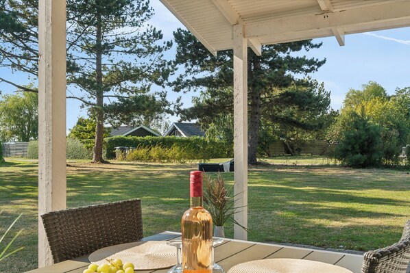 Un espace extérieur abrité, aménagé avec une table, des chaises et une bouteille de vin.