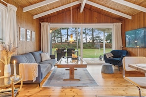 A cozy living room with a wooden ceiling, a sofa, a coffee table, and a TV mounted on the wall.