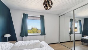A bedroom with a bed, a window with curtains, a mirror, and a ceiling light fixture. - Modern holiday home with sea view in Tejn (Allinge-Sandvig)