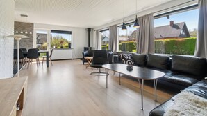 A spacious living area with a black leather sofa, a dining table, and chairs. There is a large window providing a view of the outside. - Modern holiday home with sea view in Tejn (Allinge-Sandvig)