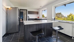 A modern kitchen with a large island, bar stools, and a view of the outdoors. - Modern holiday home with sea view in Tejn (Allinge-Sandvig)