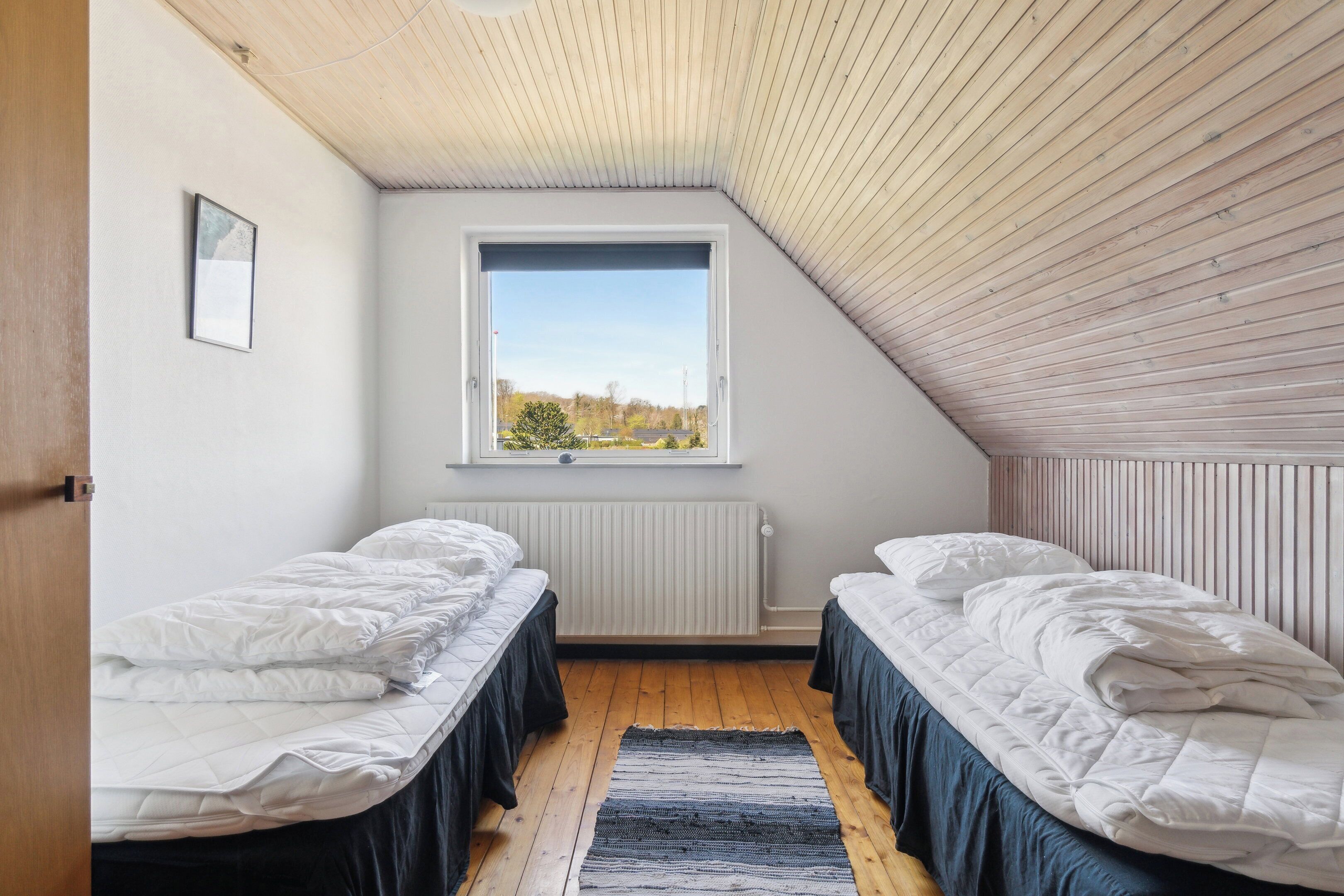 A bedroom with two beds, a window, a radiator, and a wooden ceiling.