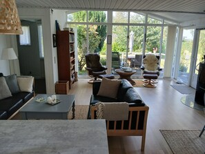 Ein geräumiges Wohnzimmer mit großem Fenster, einer Couch, einem Sessel, einem Bücherregal und einem Essbereich.