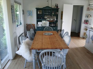 Ein Esszimmer mit Holztisch und -stühlen, einem blauen Schrank mit Gläsern und einer Tür zu einem anderen Raum.