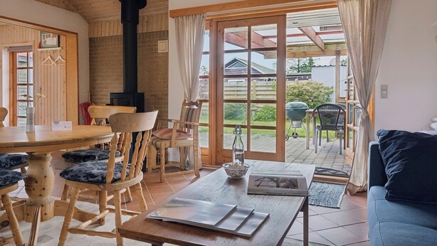 Une pièce chaleureuse avec une table en bois, des chaises, un canapé, une cheminée et une grande porte-fenêtre coulissante donnant sur un espace extérieur.