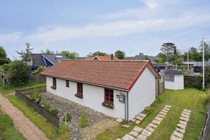 A white house with a red roof, a gravel driveway, and a wooden fence.
