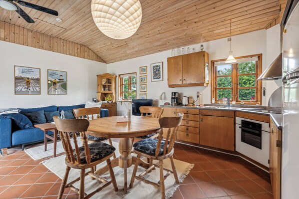 A modern kitchen with wooden cabinets, a dining table with chairs, a blue sofa, and a ceiling fan.