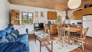 Un salon chaleureux avec un canapé bleu, une table à manger et des chaises en bois, une cuisine avec des meubles en bois et une grande fenêtre.