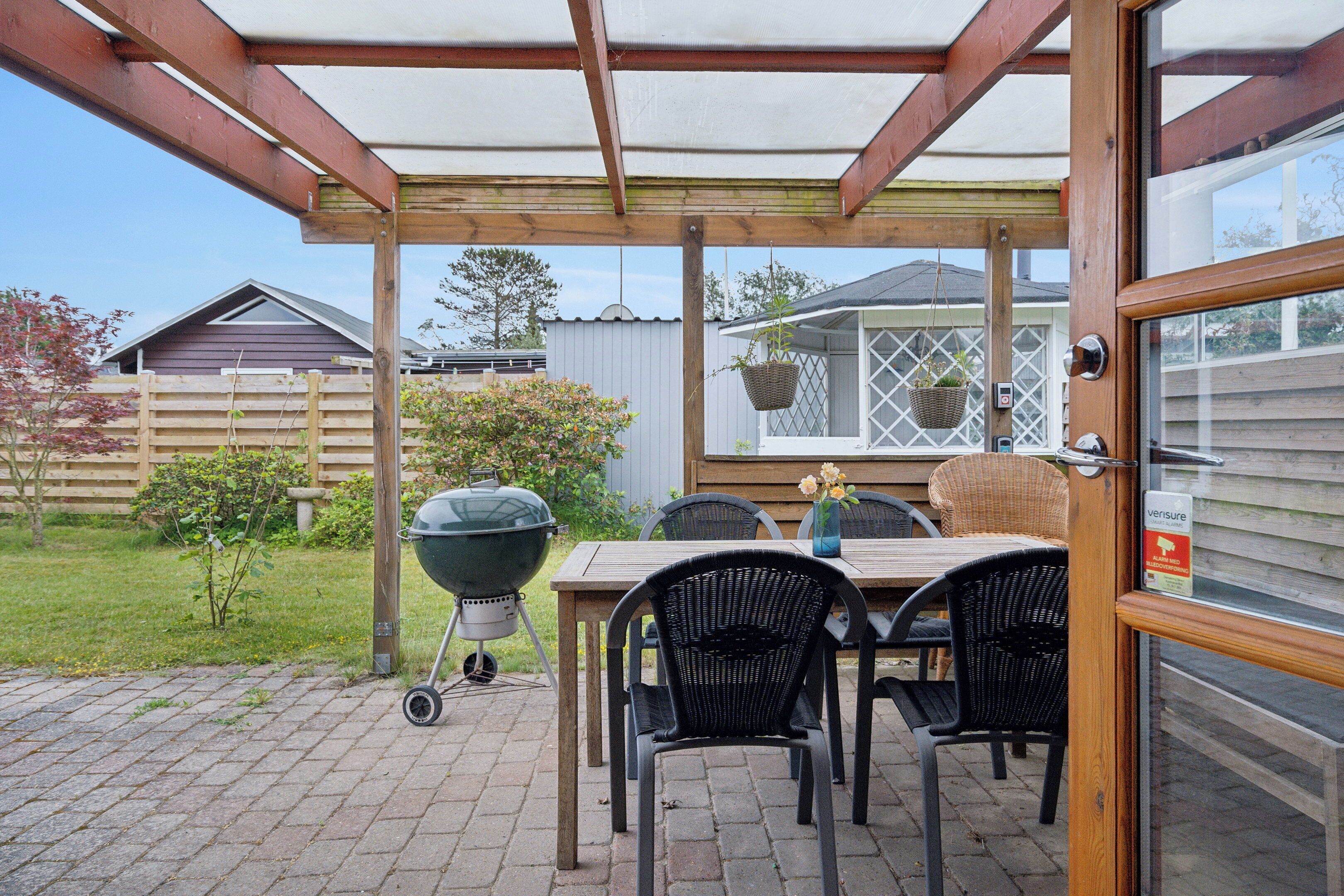A covered patio with a table and chairs, a grill, and hanging baskets.
