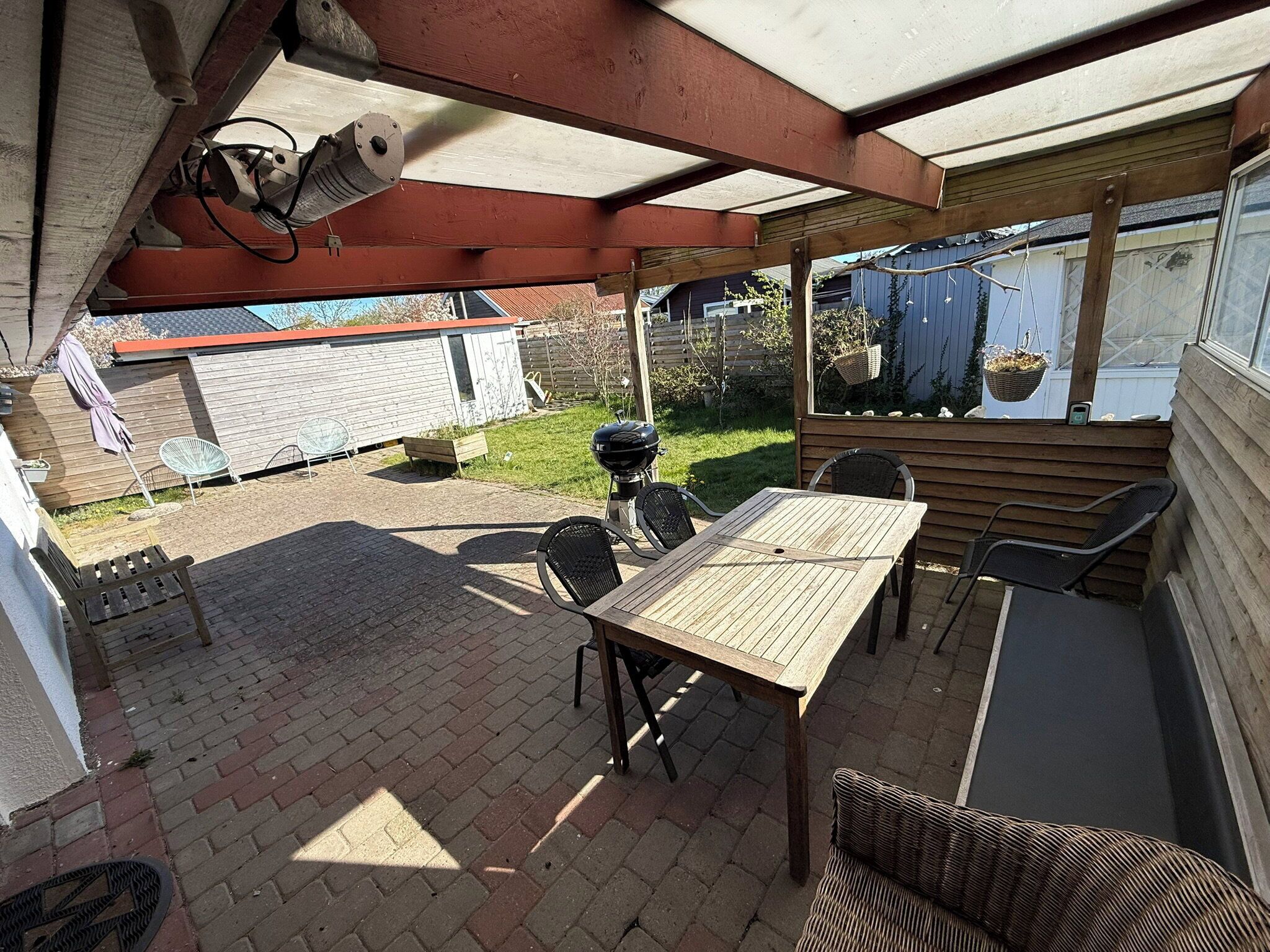 A covered patio with a table and chairs, a grill, and a hanging basket.