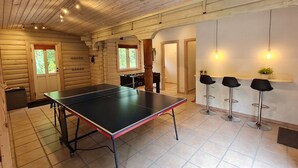 Interior de una cabaña de troncos con mesa de ping pong, mesa de futbolín y tres taburetes de bar.