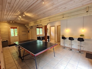 Et interiør af en træhytte med et pingpongbord, et bordfodboldbord og tre barstole.