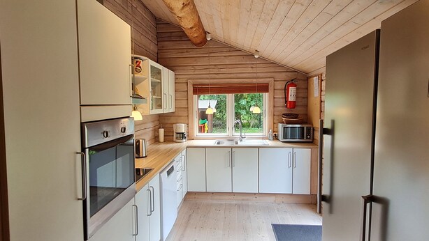 Una cocina compacta con muebles de madera, horno empotrado, microondas y fregadero.