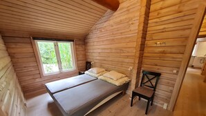 Un dormitorio de cabaña de madera con una cama, una silla y una ventana.