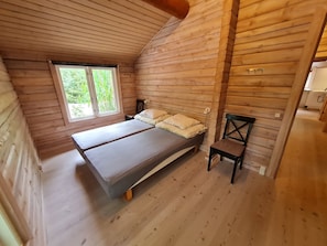 A wooden cabin bedroom with a bed, a chair, and a window.