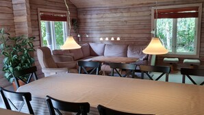Interior acogedor de una cabaña con una mesa de comedor, sillas, un sofá y dos ventanas con persianas.