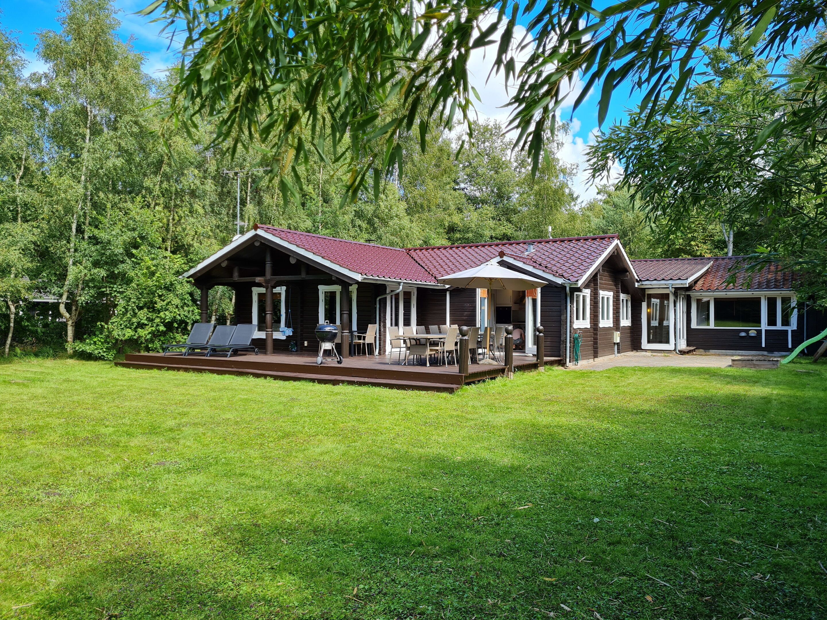 Eine Holzhütte mit überdachter Veranda, Sitzgelegenheiten im Freien und einer Grillplatz.