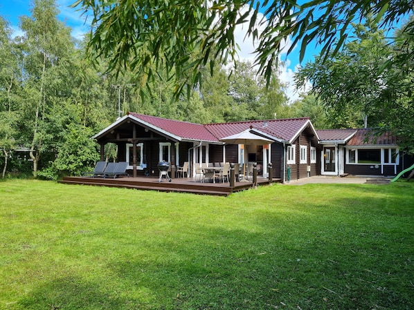 En stuga byggd av trä med en inglasad veranda, utomhusmöbler och en grillplats.