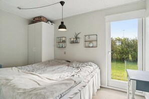 A bedroom with a bed, a desk, a wardrobe, and a window with a view of greenery.