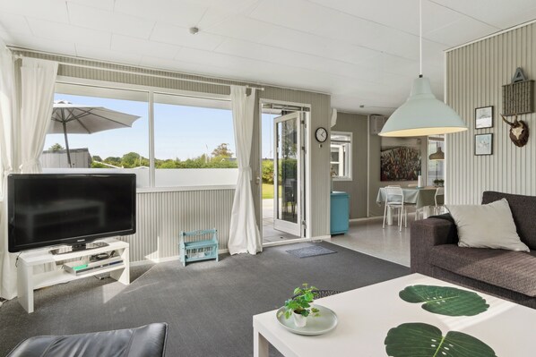 A living room with a flat-screen TV, a sofa, a coffee table with a plant, and a dining area with a table and chairs.