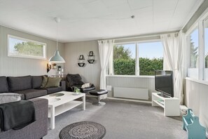 A modern living room with a sofa, coffee table, TV stand, and a view of greenery outside.