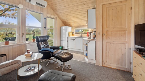 Ett rum med träpanel på väggarna, ett matbord, stolar, en soffa, en tv och en köksdel.