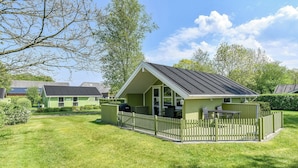 En liten, envåningsbyggnad med en inhägnad uteplats, en grill och ett bord med stolar.