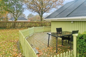 Une terrasse avec une table et des chaises, une clôture blanche en bois et, au fond, un bâtiment vert.