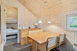 Un intérieur en bois avec des lits superposés, une table à manger, des chaises, des lampes suspendues et une fenêtre.