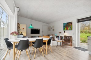Et moderne spiseområde med et hvidt bord, sorte stole, en teal-pendel og en læderstol i brunt.