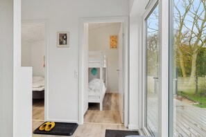 A room with a bunk bed, a door leading to another room, and a view of the outdoors through a glass door.