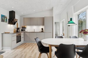 A modern kitchen with a dining area, featuring a white table, black chairs, and a green pendant light.