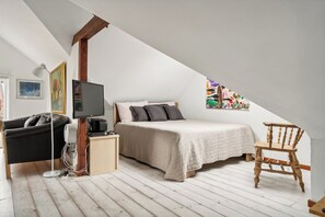 Ein Schlafzimmer mit einem Bett, einem Holzstuhl, einer schwarzen Couch, einem Fernseher und einem Bild an der Wand.