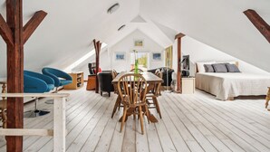 A loft-style bedroom with a sloped ceiling, a wooden dining table with chairs, a bed with pillows, and a view of the outdoors. - Lovely house with pool near charming Aarhus (Hasselager)