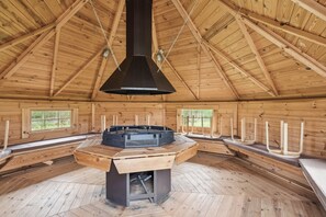 A wooden interior with a central fireplace, benches, and windows.