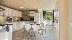 Eine moderne Küche mit weißen Schränken, Steinfliesen und einem Essbereich mit weißen Stühlen und einem Tisch.