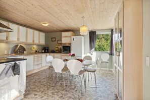 A modern kitchen with white cabinets, a stone-tiled floor, and a dining area with white chairs and a table.