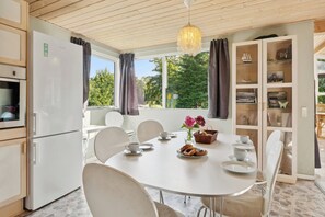 Un comedor con una mesa dispuesta para cuatro personas, un refrigerador y un armario con libros y objetos decorativos.